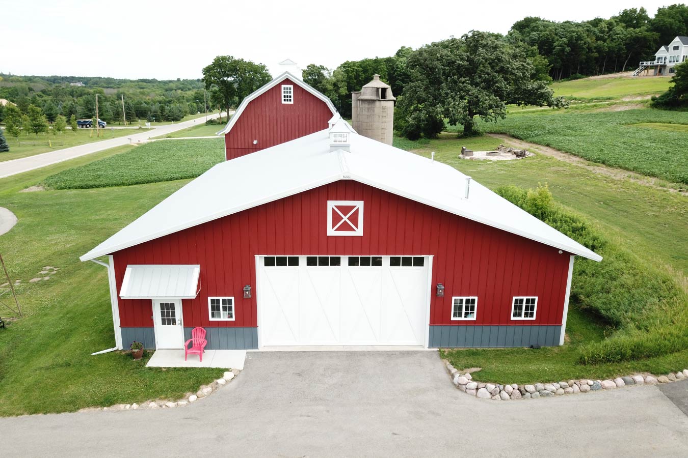 This car collection garage highlights the versatility and visual appeal of post frame construction, combining expansive storage space with a refined, barn-style design. The bold red steel siding with white trim delivers a classic look, while the gray wainscot adds durability and contrast along the base of the building. A standout feature of this car collection garage is the large overhead door, providing easy access for vehicles of all sizes. The extended row of sidewall windows allows natural light to flood the interior, making it ideal for showcasing a car collection or creating a bright workspace. The addition of cupolas along the roofline enhances both ventilation and architectural character, reinforcing the traditional aesthetic while maintaining modern functionality. Built using post frame construction, the structure offers wide-open interior spans, allowing for flexible layouts tailored to car storage, display, or hobby use. This project demonstrates how a car collection garage can be both highly functional and visually striking, delivering long-term performance with minimal maintenance.