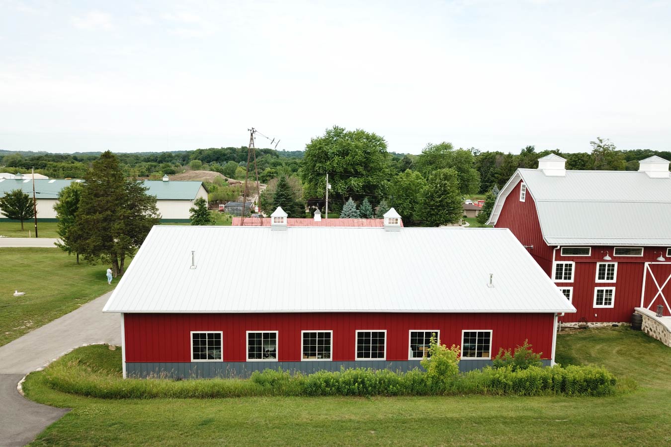 car collection garage with red steel siding, side windows, gray wainscot, and white metal roof with cupolas