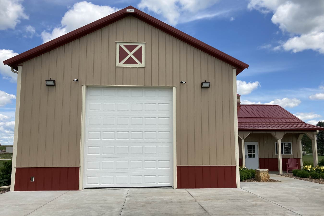 storage condo unit with large overhead door, red steel roof, and adjacent covered porch with walk door