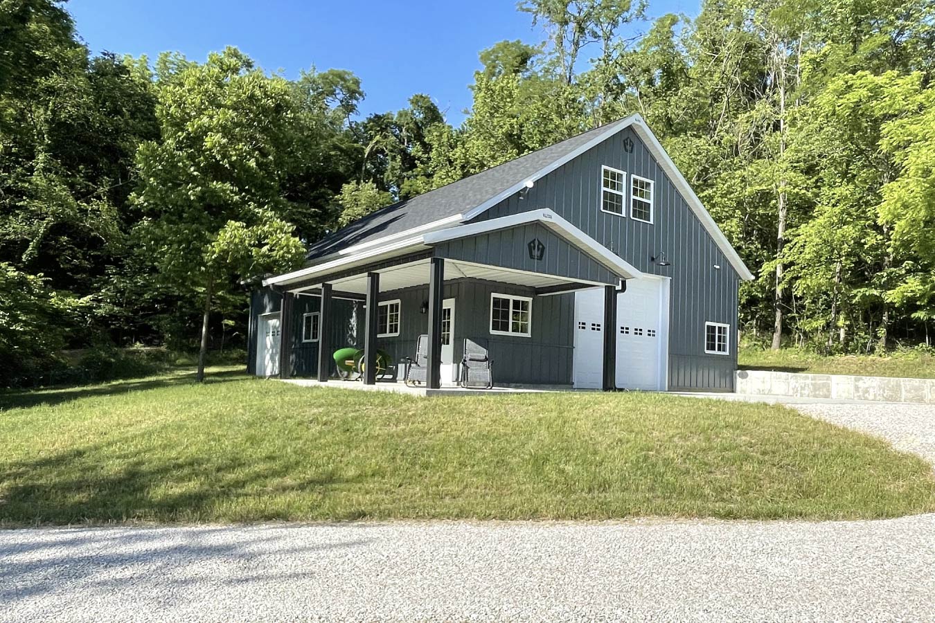 This garage with living quarters showcases a functional and visually appealing post frame design, combining garage storage with comfortable upper-level living space. The main level features a large overhead garage door for easy access, while the upper loft provides additional living or workspace. As with all Walters Buildings projects, both the siding and roof are constructed from steel (unless otherwise specified), ensuring long-lasting durability and minimal maintenance. The post frame construction allows for wide-open interior spans, maximizing usable space for both garage and living areas. A standout feature of this garage with living quarters is the covered porch, creating a welcoming outdoor space perfect for relaxing or entertaining. Multiple windows provide natural light throughout the building, enhancing both functionality and comfort. This garage with living quarters demonstrates how post frame construction can seamlessly combine storage, workspace, and residential living into one efficient and attractive structure.