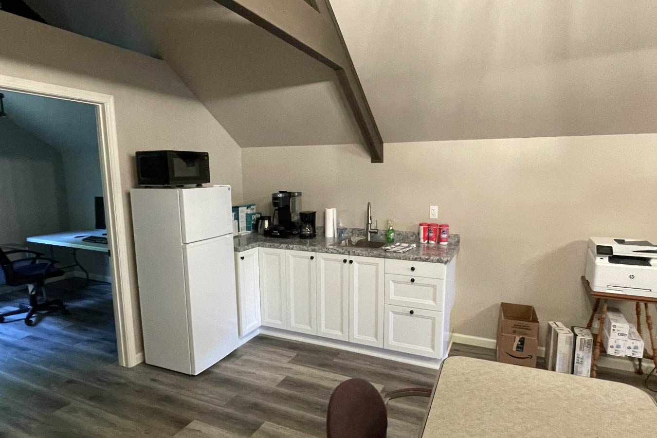 This interior loft of a garage with living quarters highlights the spacious and functional design made possible through post frame construction. The open floor plan features exposed wood beams, creating a warm, inviting atmosphere while maximizing structural efficiency and visual appeal. As with all Walters Buildings projects, both the siding and roof are constructed from steel (unless otherwise specified), ensuring long-term durability on the exterior while allowing for fully finished and comfortable interiors. The post frame system enables wide-open spans without load-bearing walls, giving flexibility for layout and use. The space includes durable wood-style flooring, a kitchenette area, and ample room for dining, office work, or relaxation. Natural light flows in through rear windows and doors, enhancing the livability of the loft. This garage with living quarters interior showcases how post frame construction can seamlessly blend garage functionality below with a comfortable and efficient living space above.