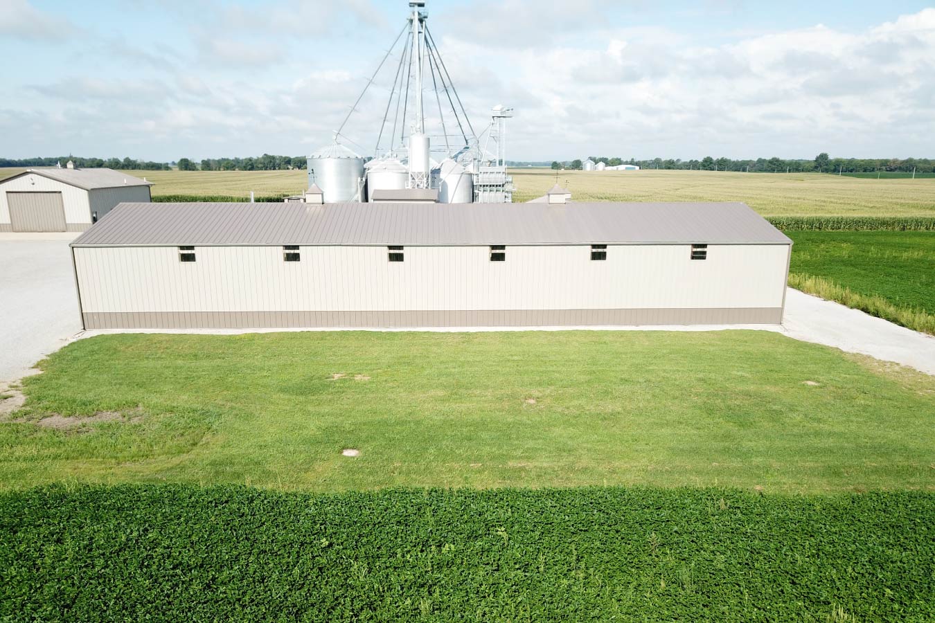Long grain farm pole barn used as an agricultural storage building near grain bins with natural light windows
