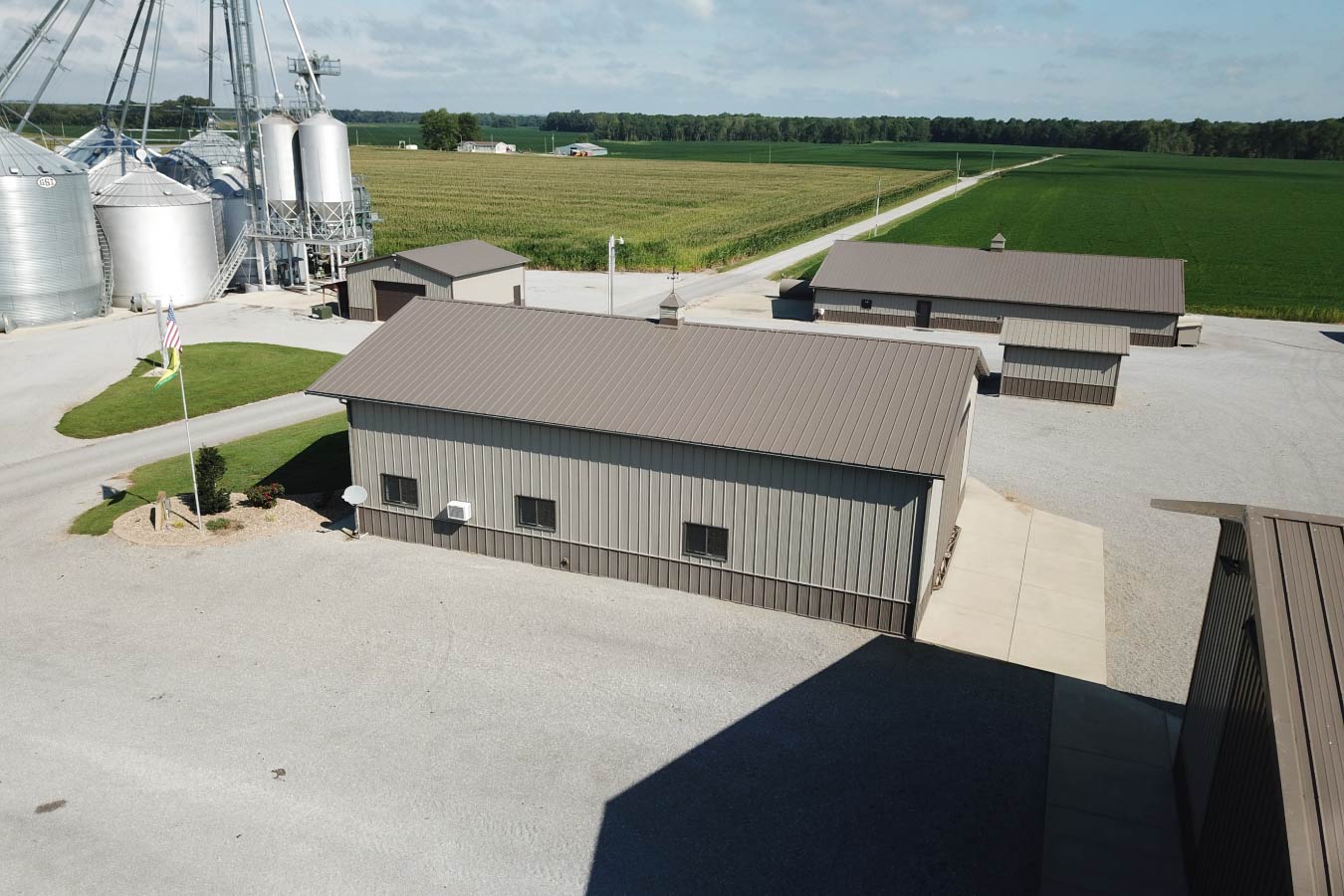 Side view of grain farm pole barns used as agricultural storage buildings beside grain bins and crop fields