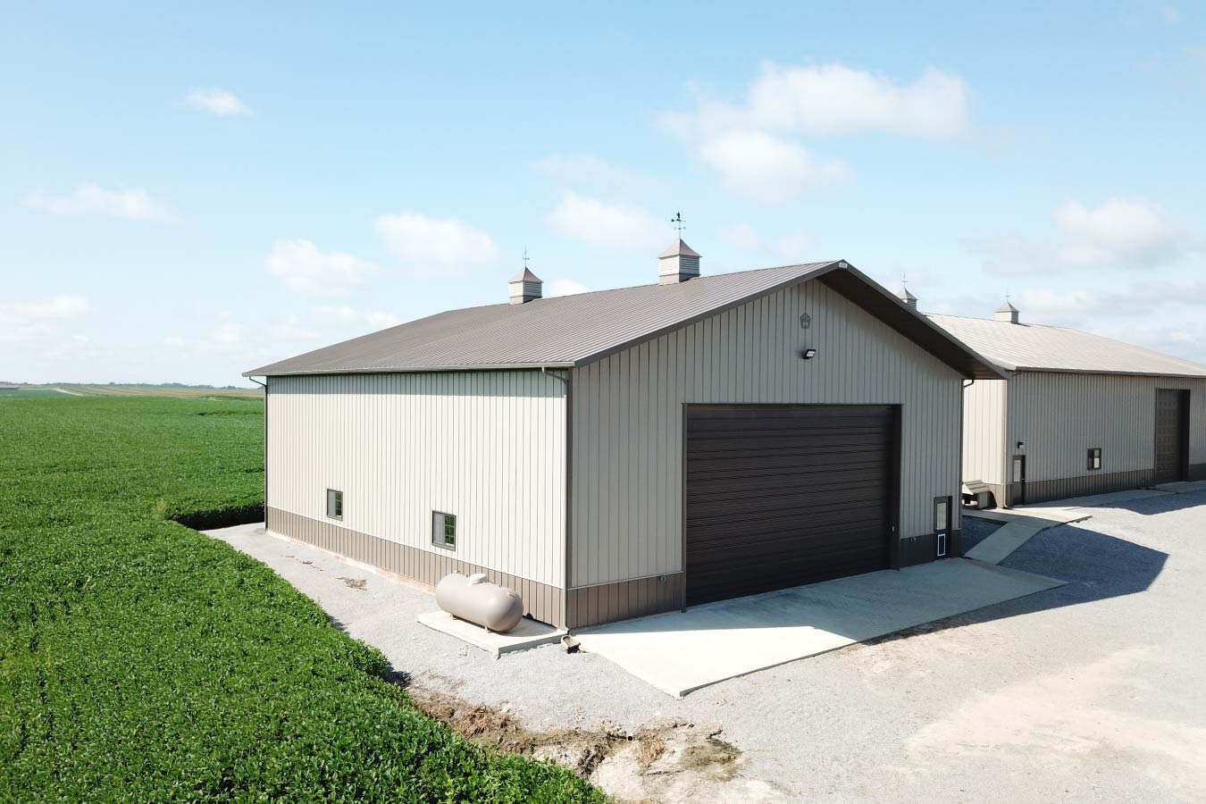 Large agricultural pole barn used as a farm equipment storage building beside crop fields with overhead door.