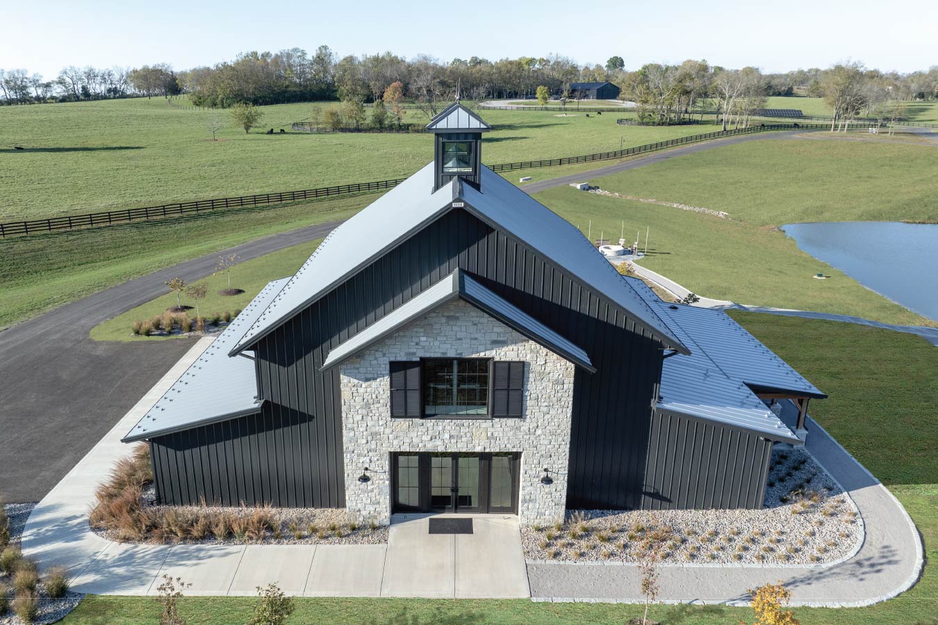 Front view of the Keene Ranch event barn featuring black steel siding, stone facade, cupola, and glass entry doors. Galvalume Roof