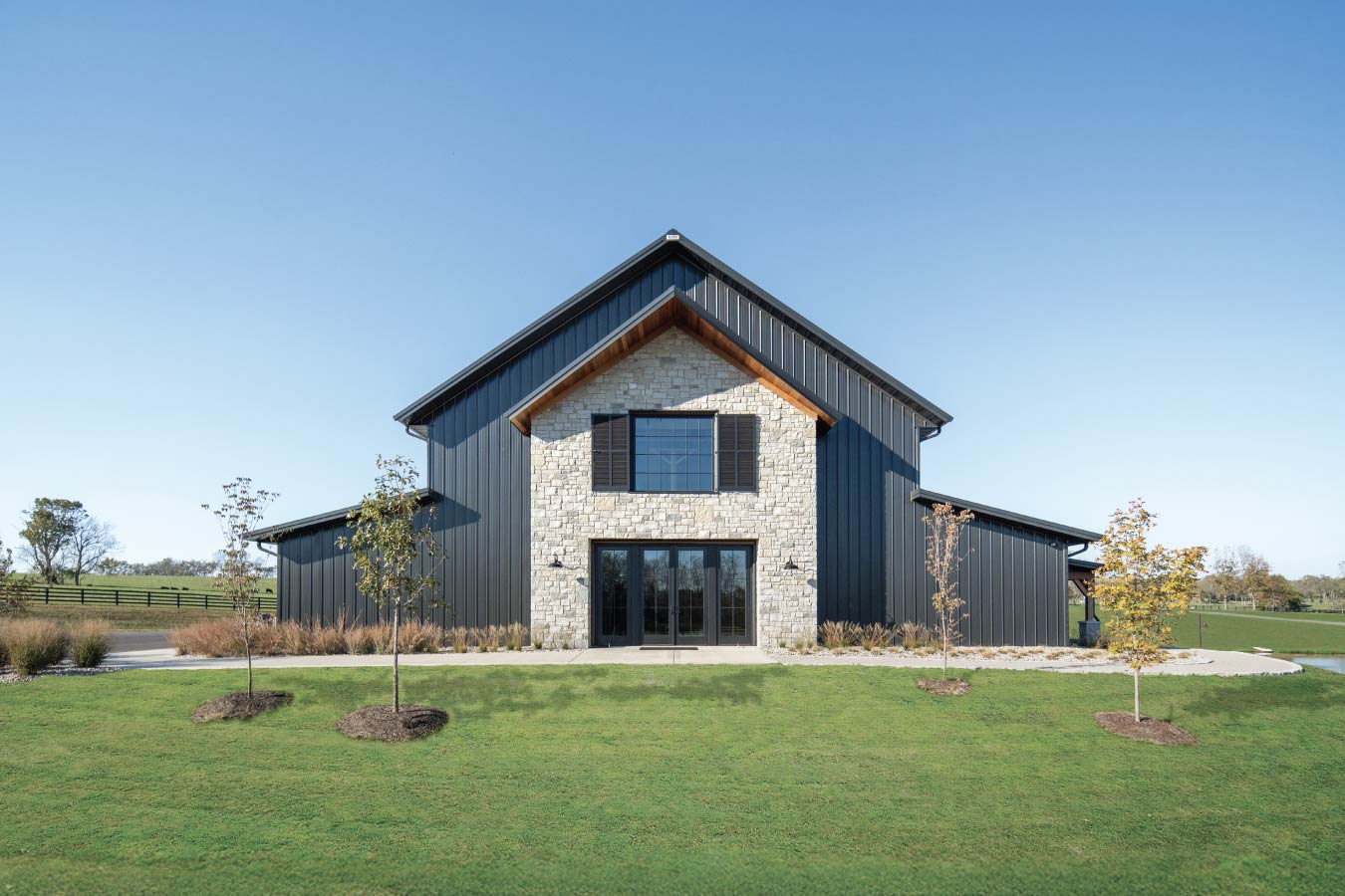 Front view of the Keene Ranch event barn with black steel siding, stone facade, large windows, and landscaped lawn. Masonry Front Entrance