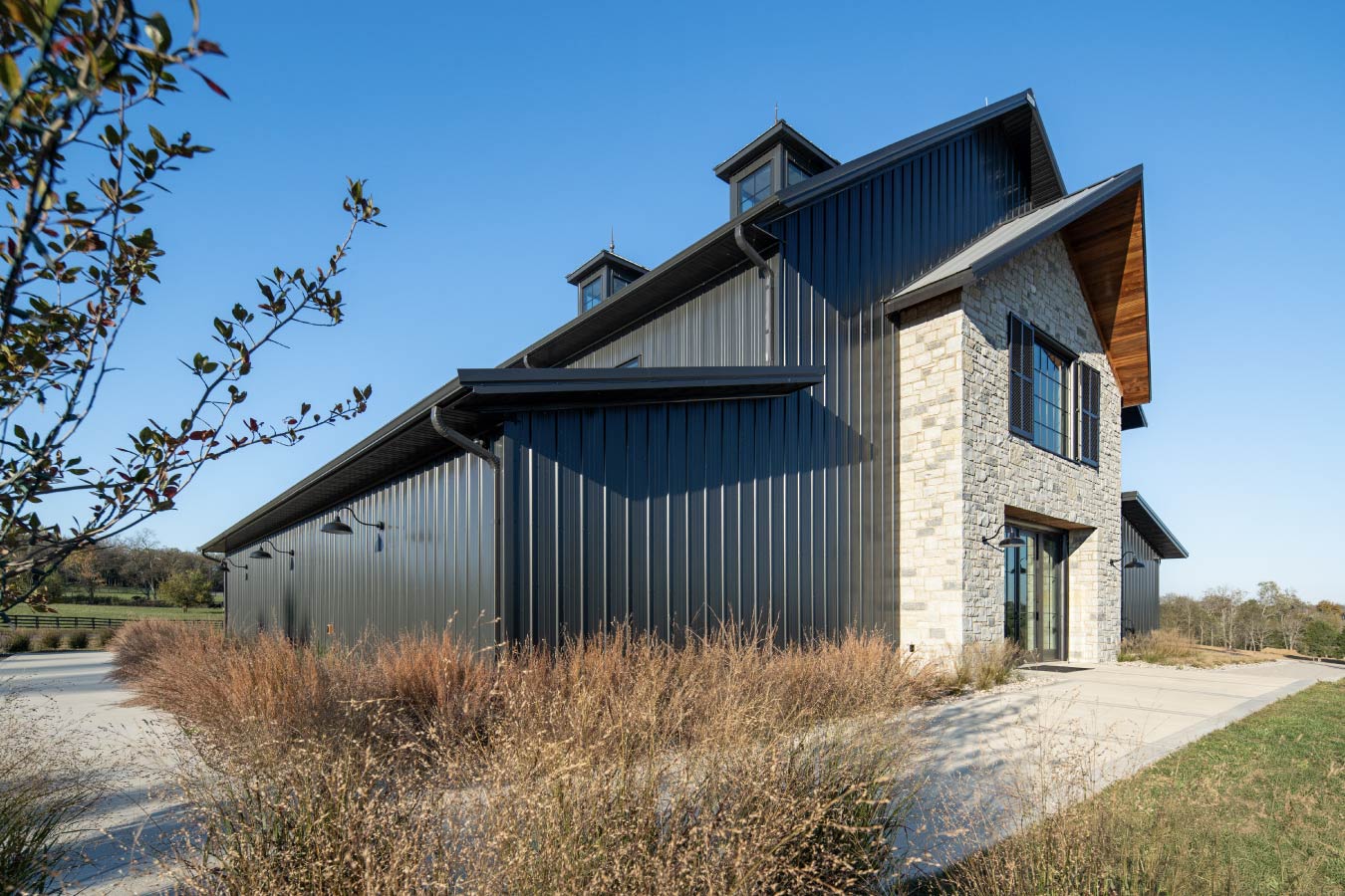 Keene Ranch event barn exterior with black steel siding, stone entry tower, metal roof, and decorative cupolas. Walkway to Event Barn