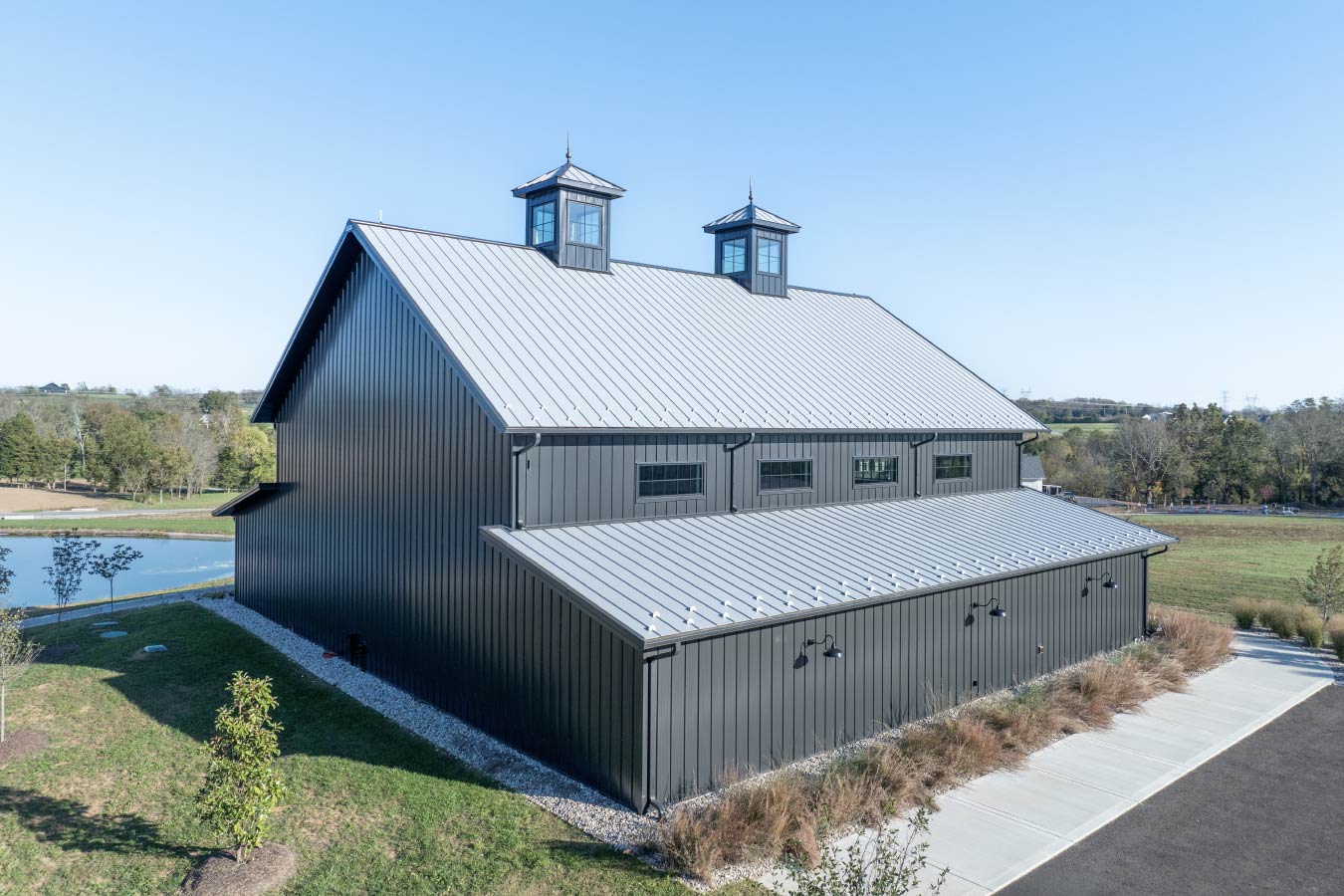 Rear exterior of the Keene Ranch event barn with black steel siding, metal roof, clerestory windows, and dual cupolas. Rear View