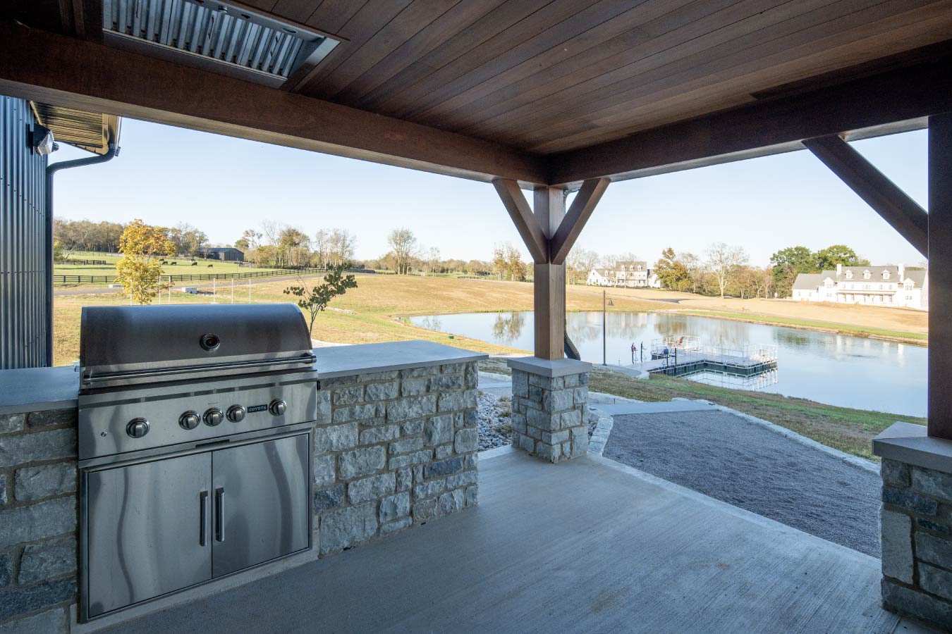 Covered patio at the Keene Ranch event barn with outdoor kitchen, stone counter, and views of a pond and countryside. Grill overlooking Pond