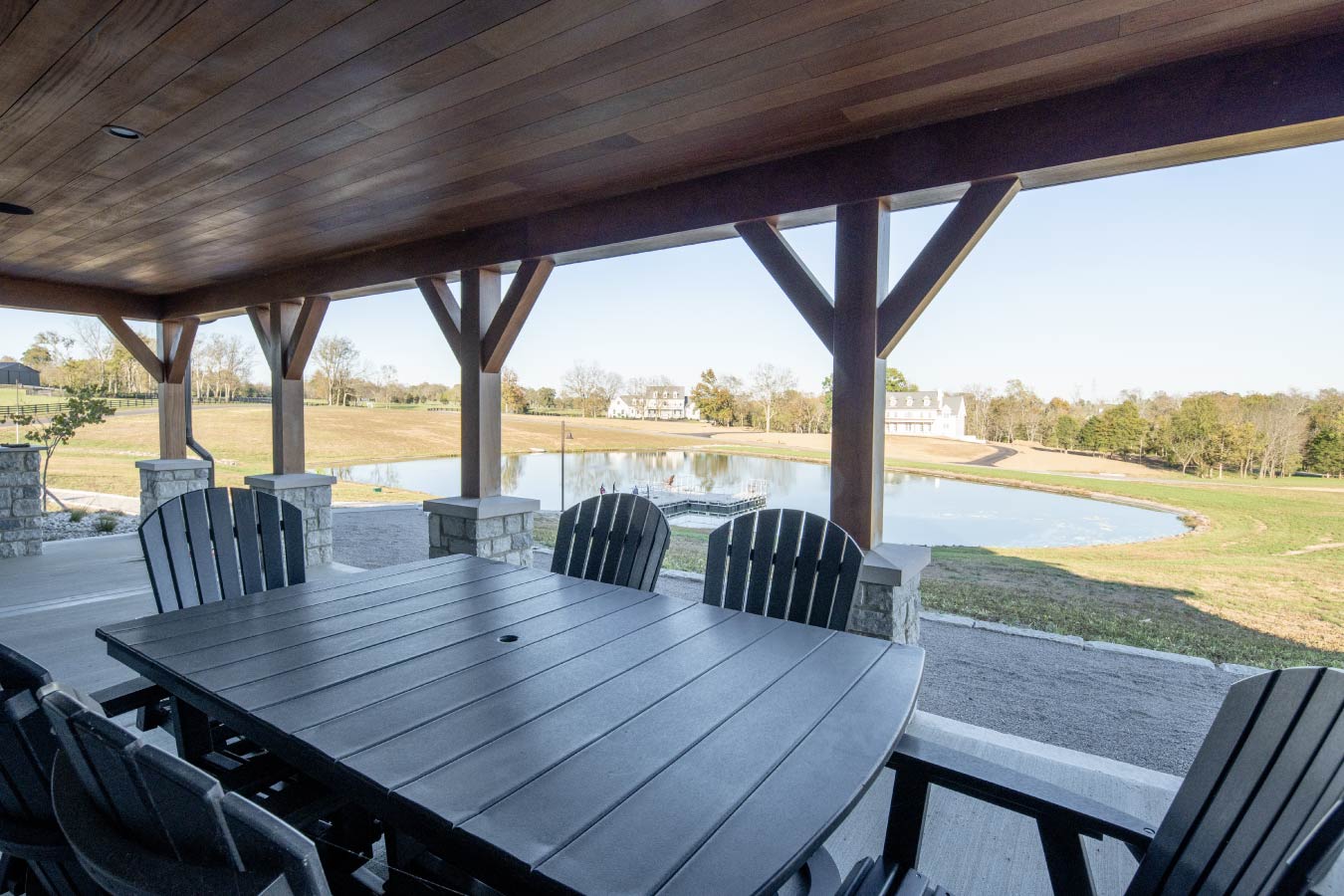 Covered patio dining area at the Keene Ranch event barn with timber posts, outdoor table, and pond views.