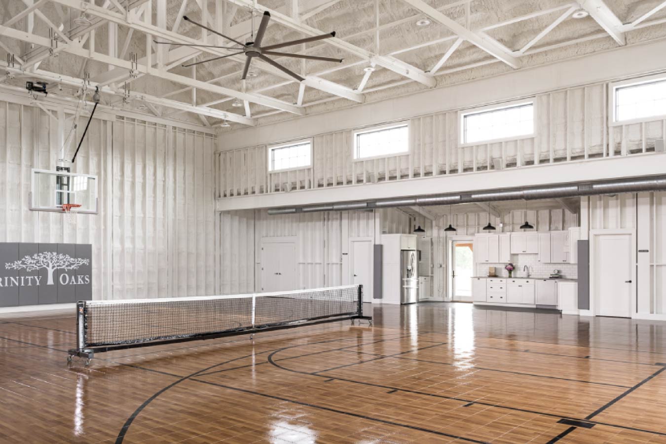 Interior of the Keene Ranch event barn with recreation court, pickleball net, kitchen area, and exposed white trusses. Indoor Sports Court