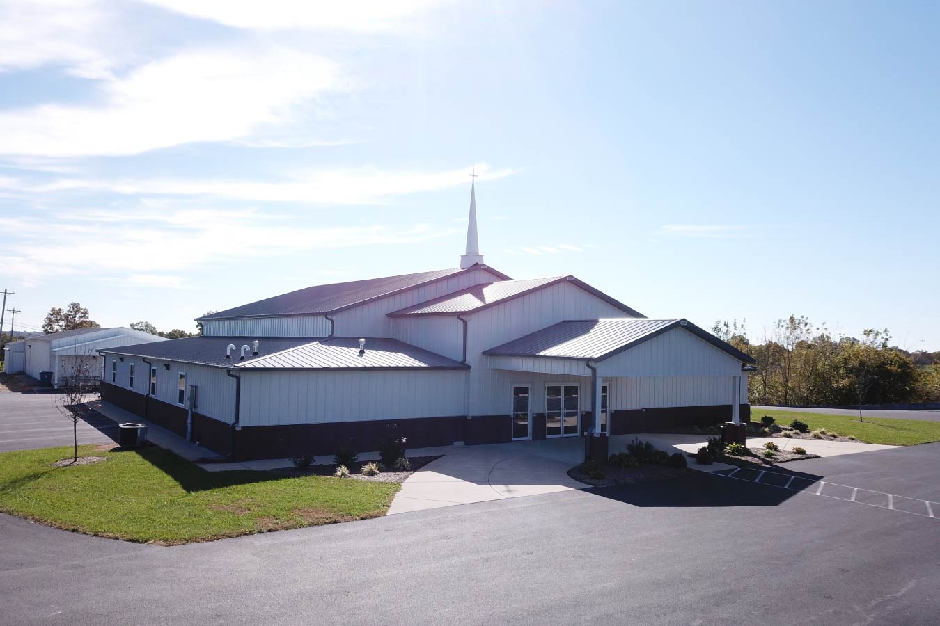 Pleasant Hill Christian Church post frame church building with white steel siding, brick wainscot, gray metal roof, and steeple. Front View of Church Building