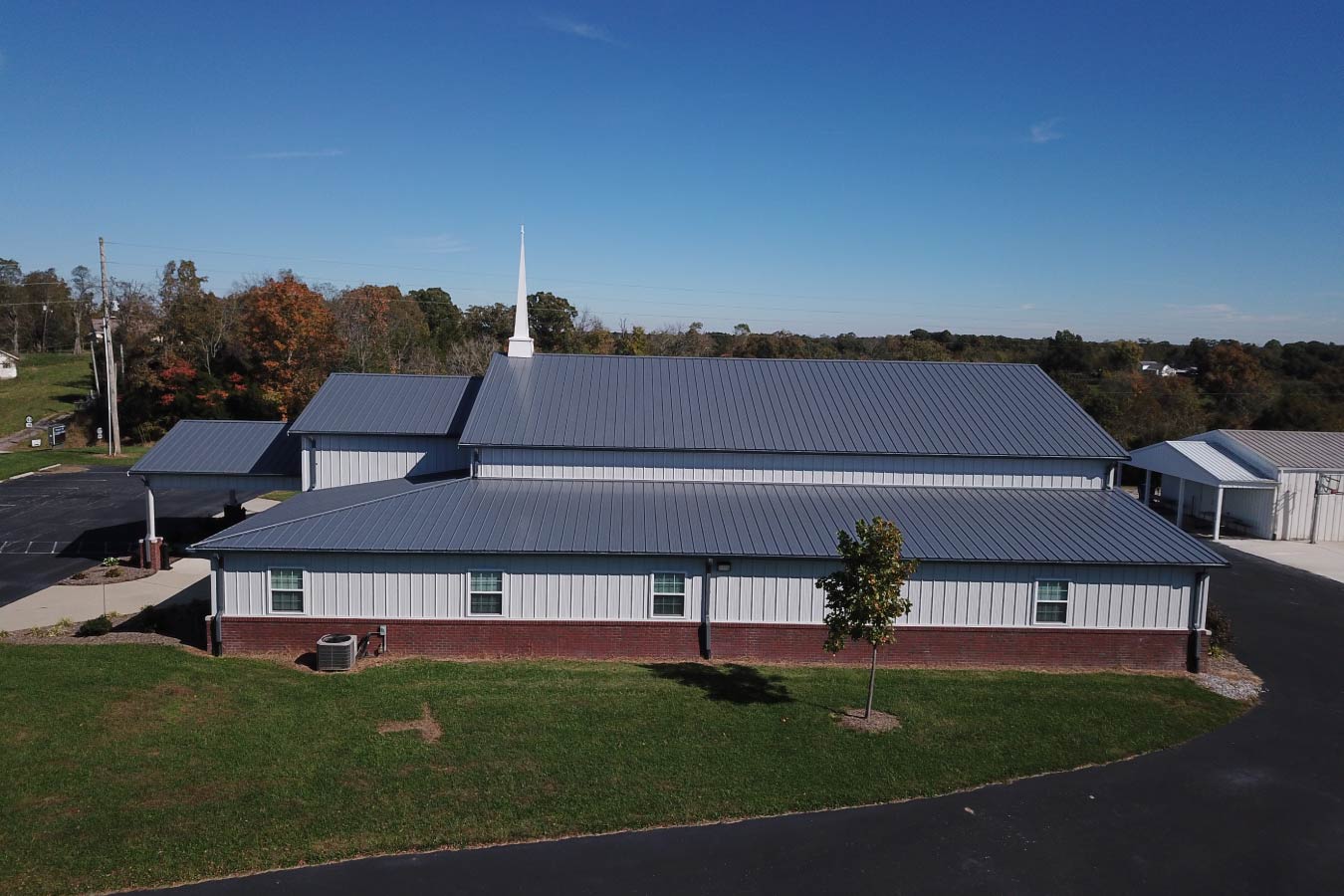 Pleasant Hill Christian Church post frame church with white steel siding, brick wainscot, gray metal roof, and steeple.
