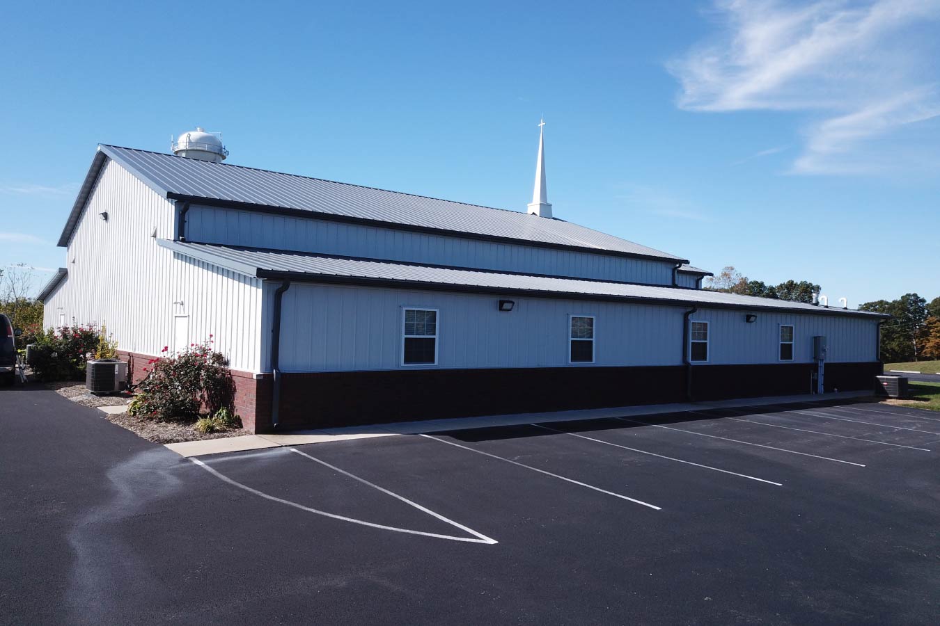 Side view of Pleasant Hill Christian Church with white steel siding, red brick wainscot, gray metal roof, and steeple.
