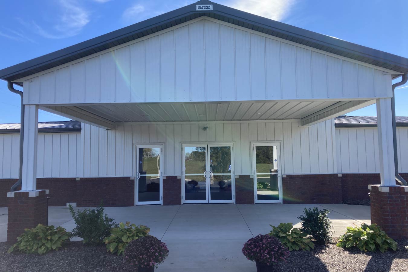 Covered entrance canopy of Pleasant Hill Christian Church with white steel siding, brick wainscot, and glass entry doors.
