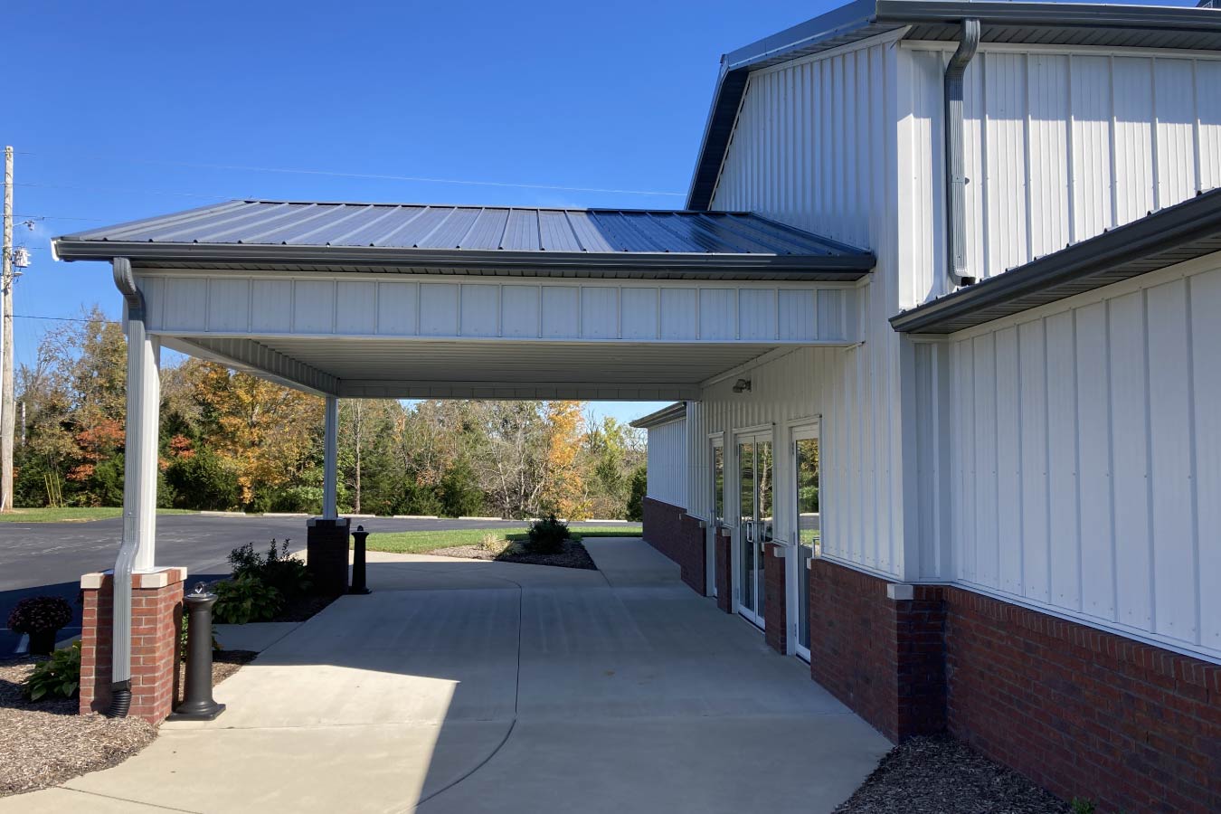 Covered entrance canopy at Pleasant Hill Christian Church with white steel siding, brick wainscot, and metal roof.
