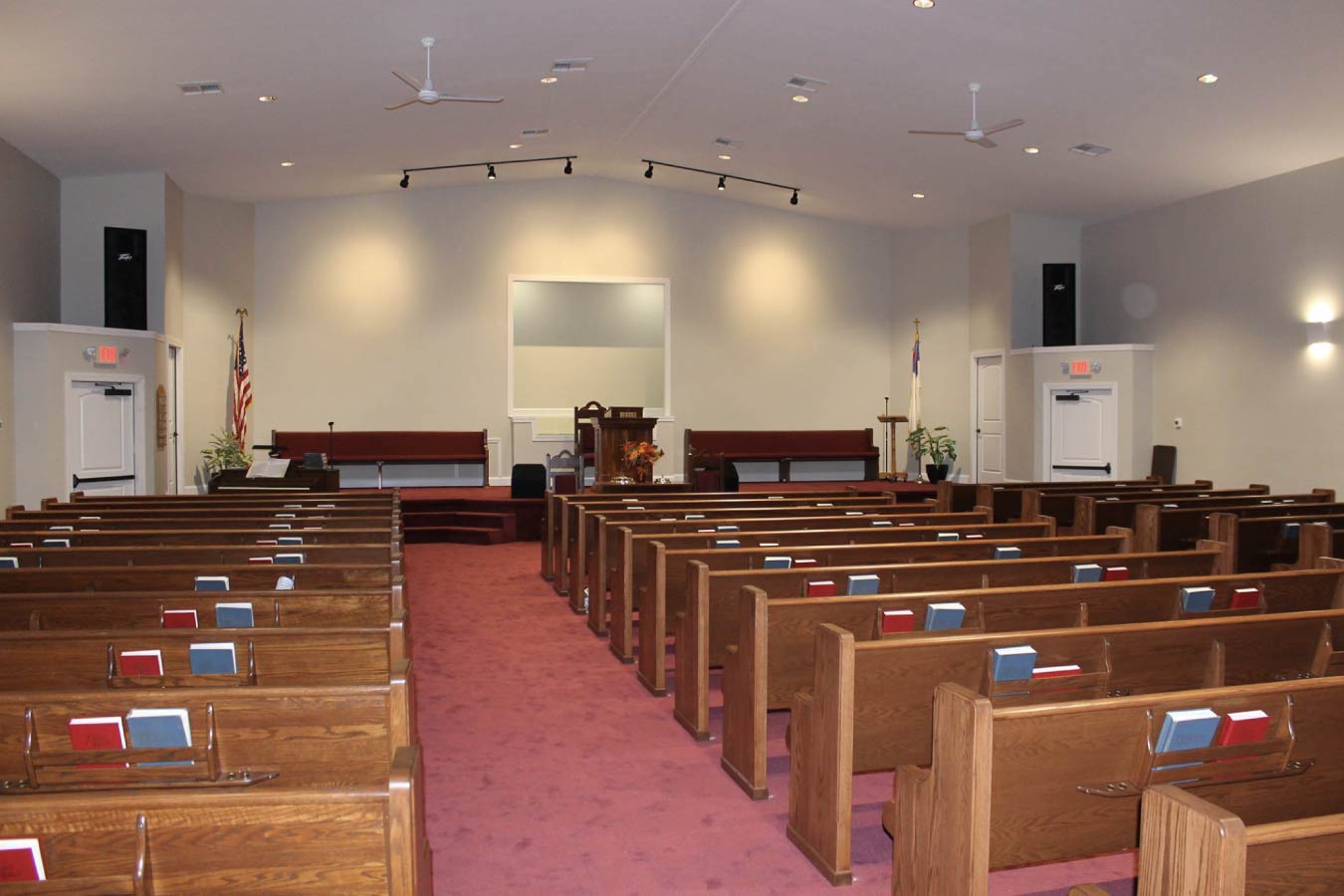 Church sanctuary interior with wooden pew seating, pulpit stage, red carpet aisle, and modern lighting