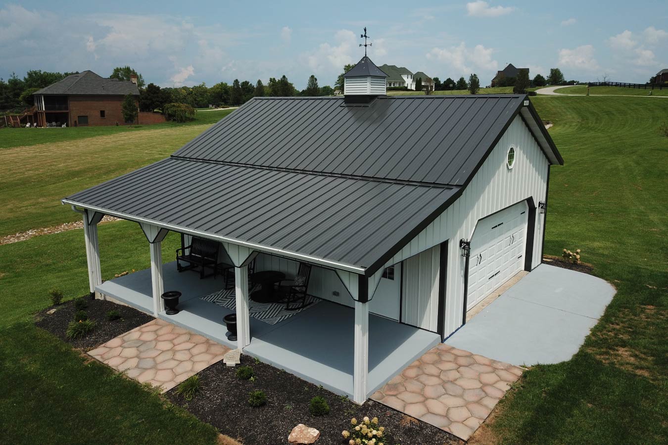 pole shed with covered porch, white steel siding, black trim, gray metal roof, and cupola with weathervane