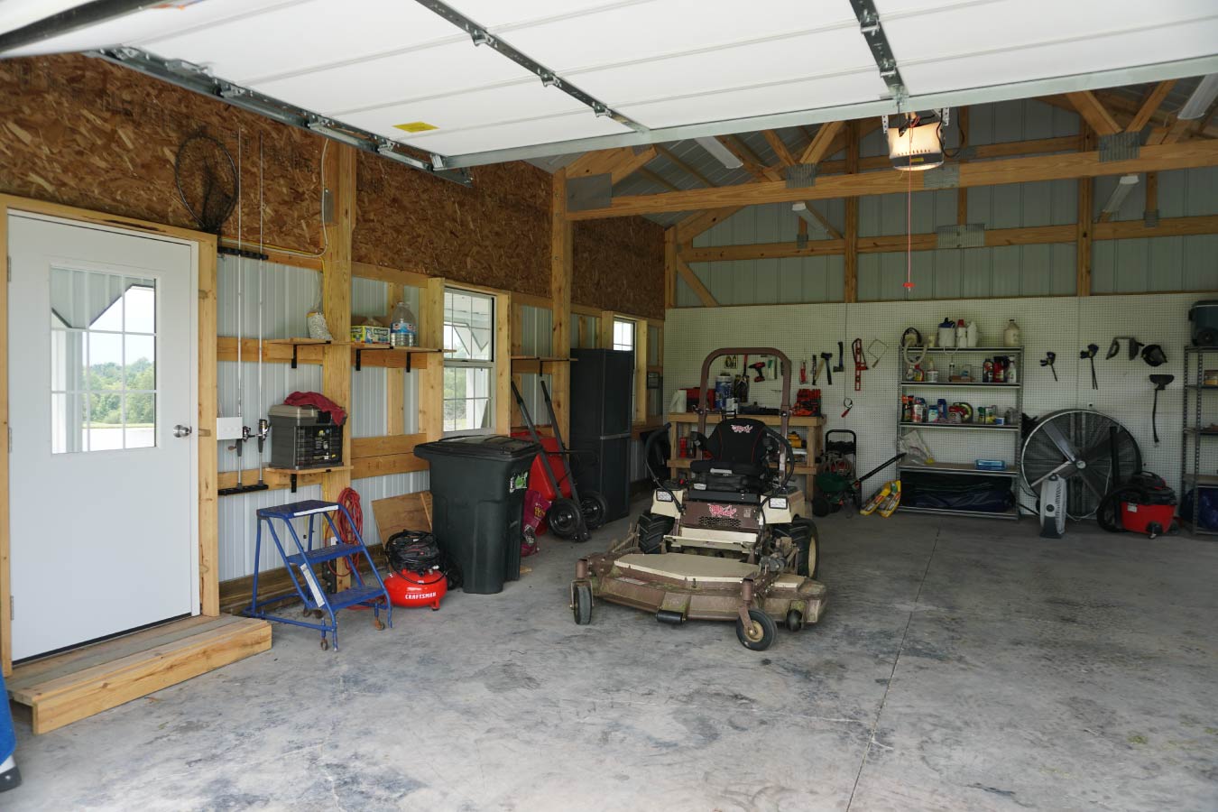 pole shed interior with exposed post frame construction, concrete floor, overhead door, and workshop storage