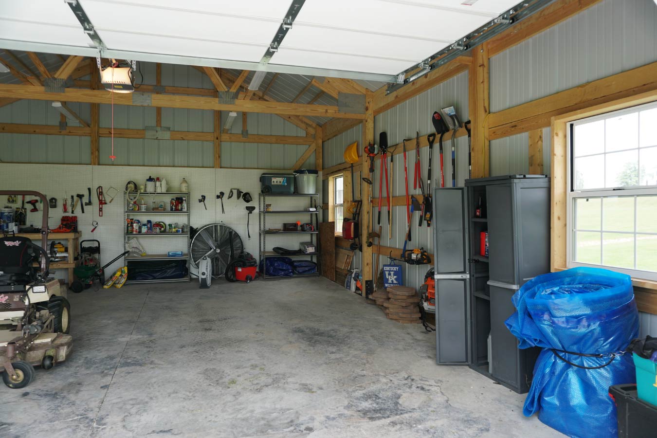 pole shed interior with exposed post frame construction, concrete floor, overhead door, and workshop storage