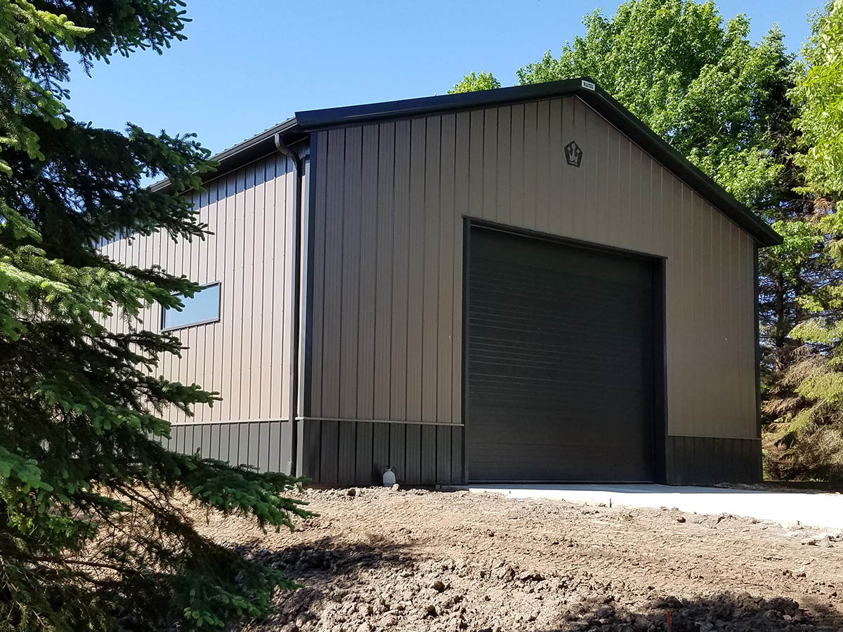 Steel equipment storage building with large overhead door, wainscot siding, and window in rural setting