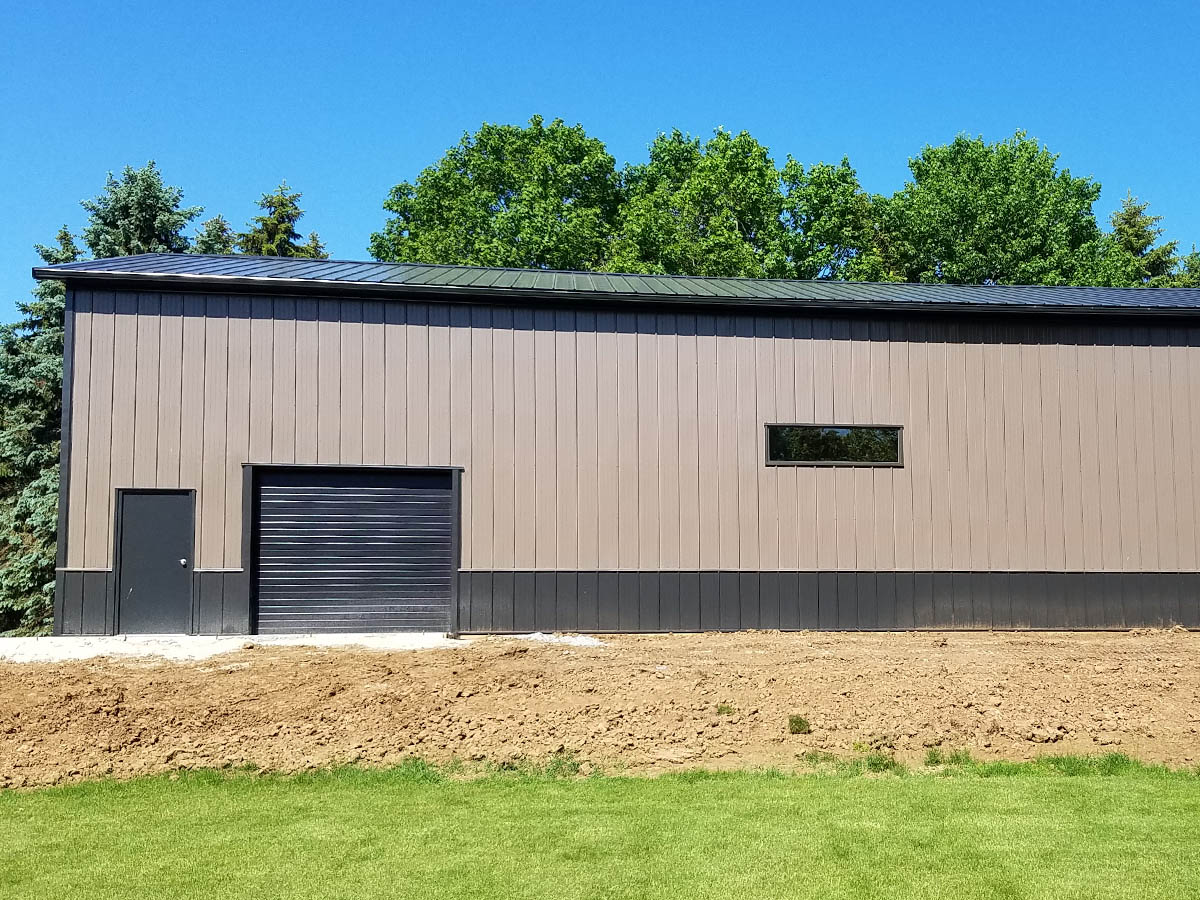 Steel equipment storage building with overhead door, walk door, horizontal window, and wainscot siding