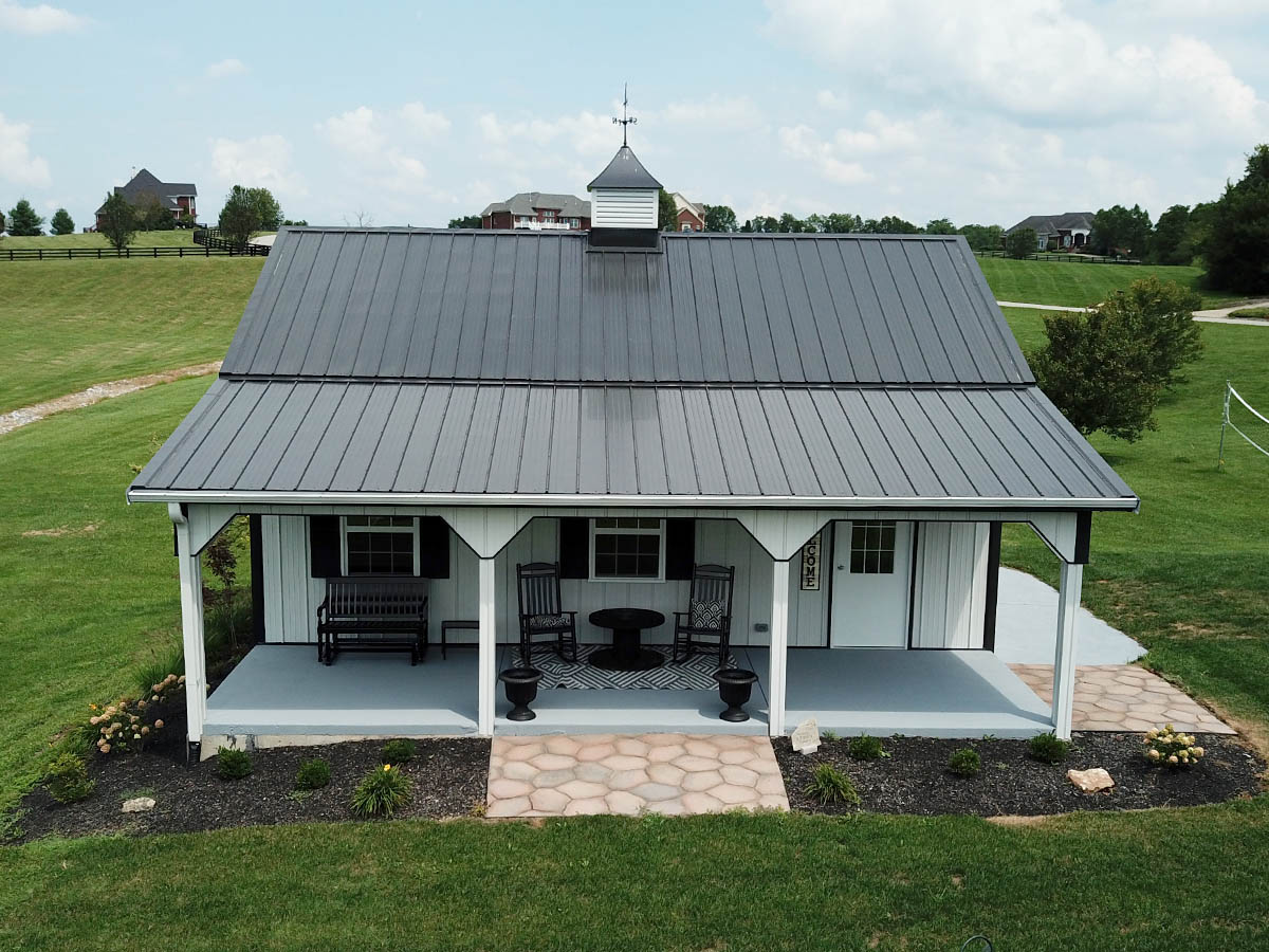 Post frame building with steel siding, full length covered porch, and cupola