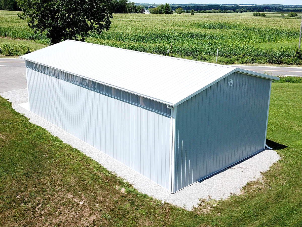 Steel agricultural storage building with long horizontal windows and gravel base in rural farmland setting