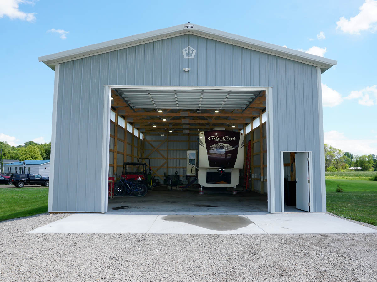 Steel post frame building with large overhead door open showing RV storage interior and walk door entrance