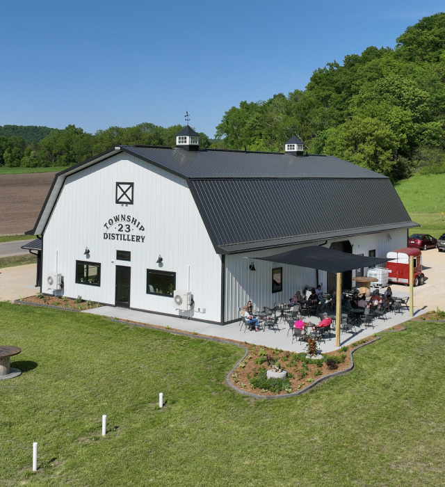 commercial building distillery with black gambrel roof white siding and outdoor patio seating commercial building distillery with black gambrel roof white siding and outdoor patio seating