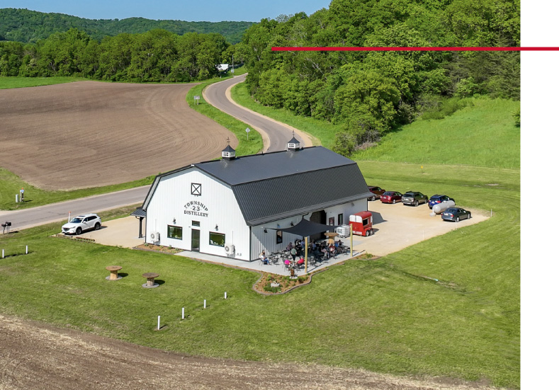 commercial building distillery with gambrel roof outdoor patio seating rural landscape and parking area commercial building distillery with black gambrel roof white steel siding cupolas and covered entrance canopy