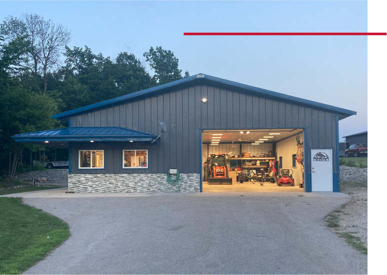 Lake House Garage with Open Bay and Covered Porch Entry | Walters Buildings Lake house garage exterior at dusk with open overhead door and lit interior workspace