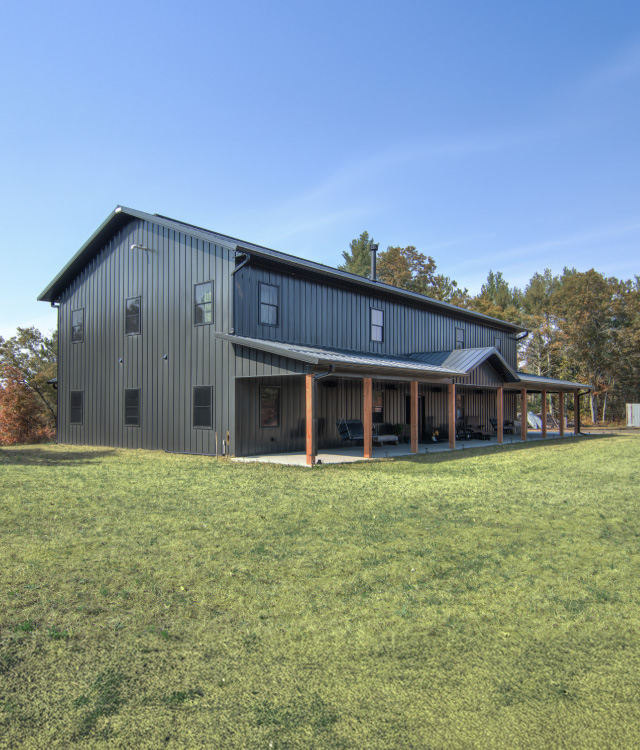 Modern Barndominium with Covered Porch | Walters Buildings Barndominium with dark steel siding, metal roof, and covered wraparound porch