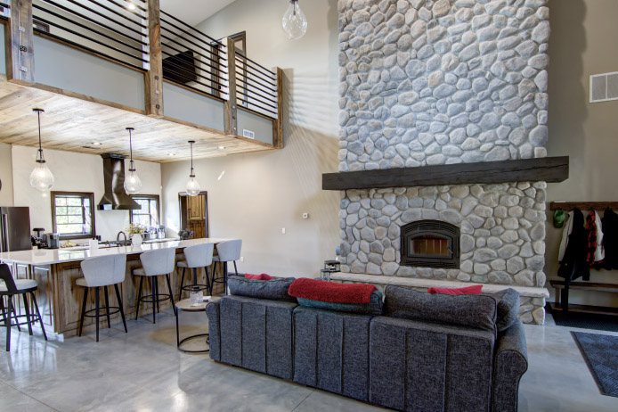 Barndominium Interior with Stone Fireplace and Loft | Walters Buildings Barndominium interior with tall stone fireplace, open kitchen, and loft balcony