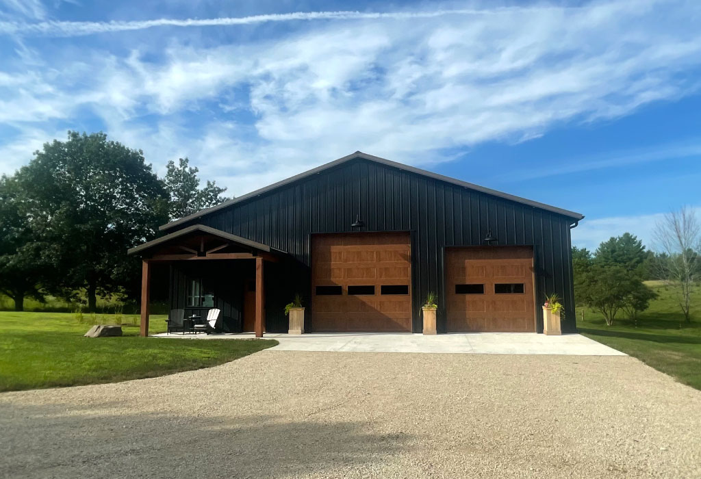 Post Frame Garage with Covered Porch and Wood Overhead Doors Post frame garage with black steel siding, wood overhead doors, and covered porch entrance