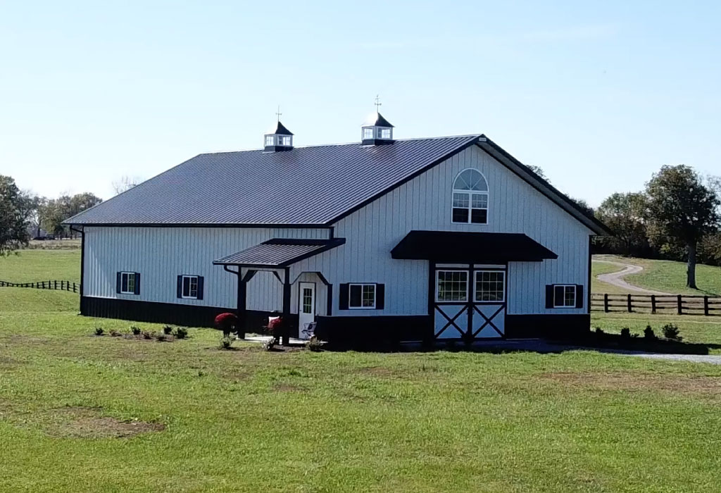 Steel horse barn with cupolas, covered entry porch, sliding barn doors, and residential-style windows