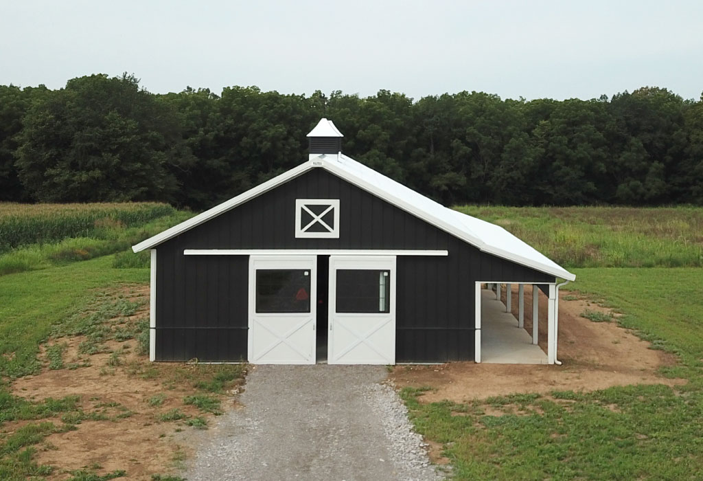 Post frame horse barn with steel siding, sliding doors, cupola, and lean to addition