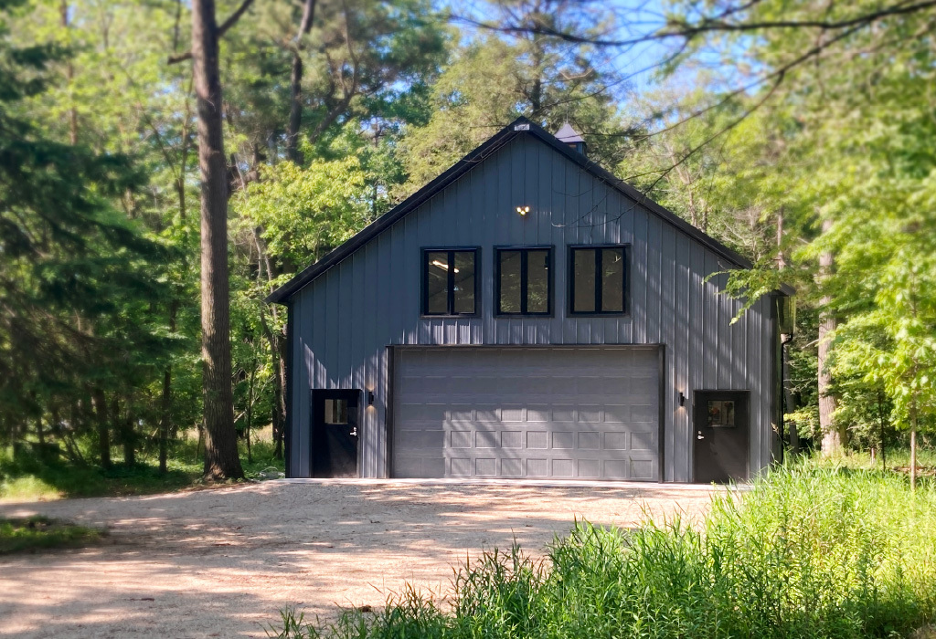 Post-Frame Storage Building Garage with Overhead Door and Upper Windows Post-frame storage building garage with steel siding, overhead door, upper windows, and wooded setting
