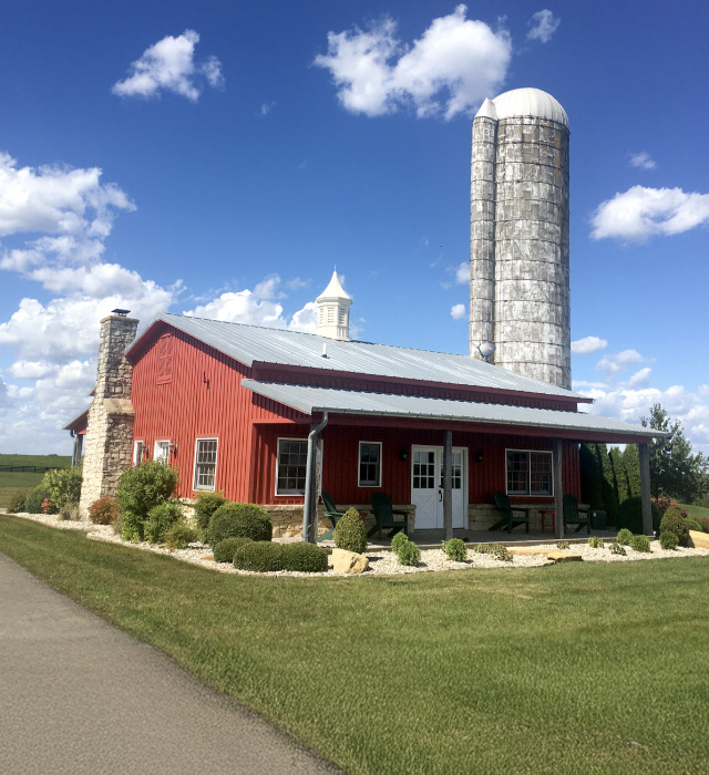 Pole barn house with red steel siding, metal roof, covered porch, and stone chimney Barn House with Silo in Crestwood Kentucky