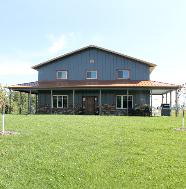 Pole barn house with wraparound porch, stone wainscot, and copper metal roof built by Walters Buildings Pole Barn House in Spring Valley, Wisconsin