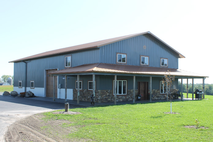 Pole barn house with wraparound porch, copper metal roof, and stone wainscot by Walters Buildings