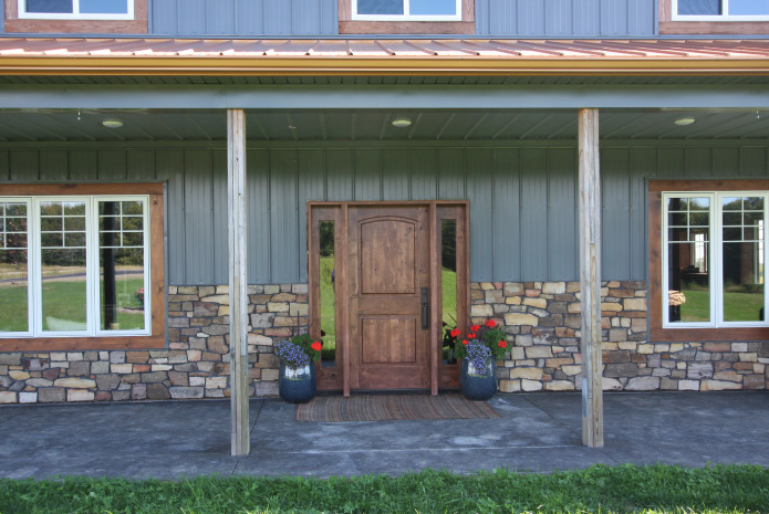 Pole barn house front entrance with wood door, stone wainscot, and covered porch