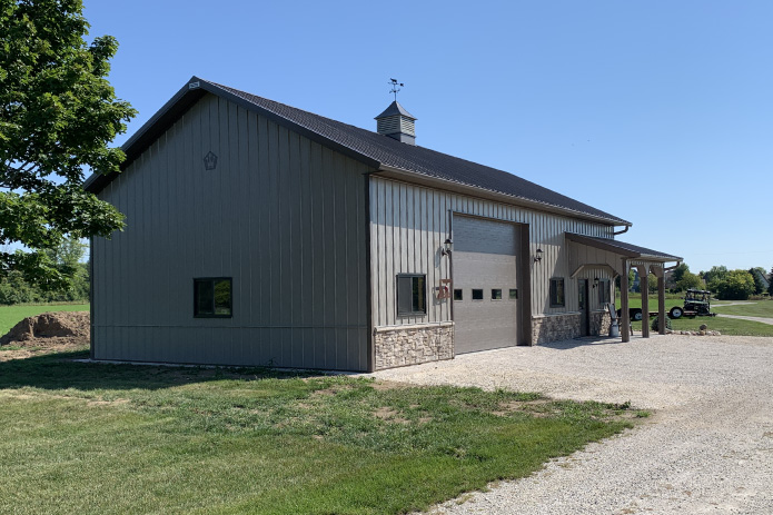 Residential Workshop with Garage Door and Covered Porch | Walters Buildings Residential workshop with steel siding, steel roof, overhead garage door, stone wainscot, and covered porch