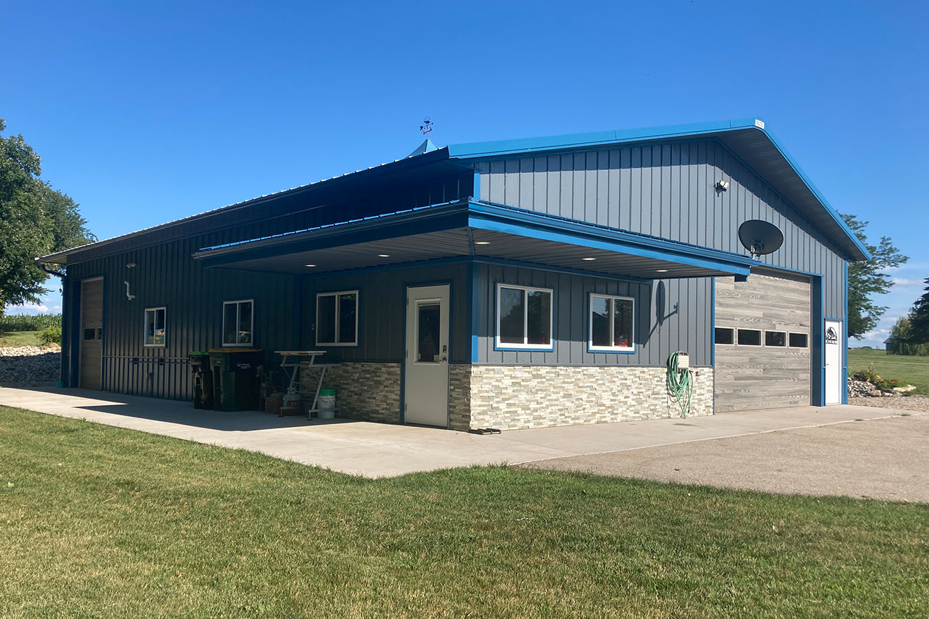 95-1191 Lake house garage with blue steel siding, stone wainscot, covered patio, and overhead garage door