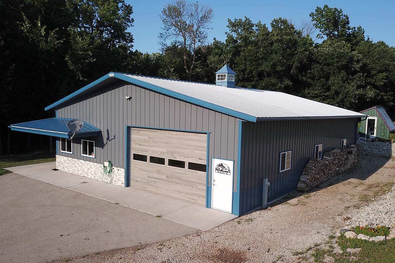 Lake house garage with gray steel siding, blue trim, cupola, and overhead garage door