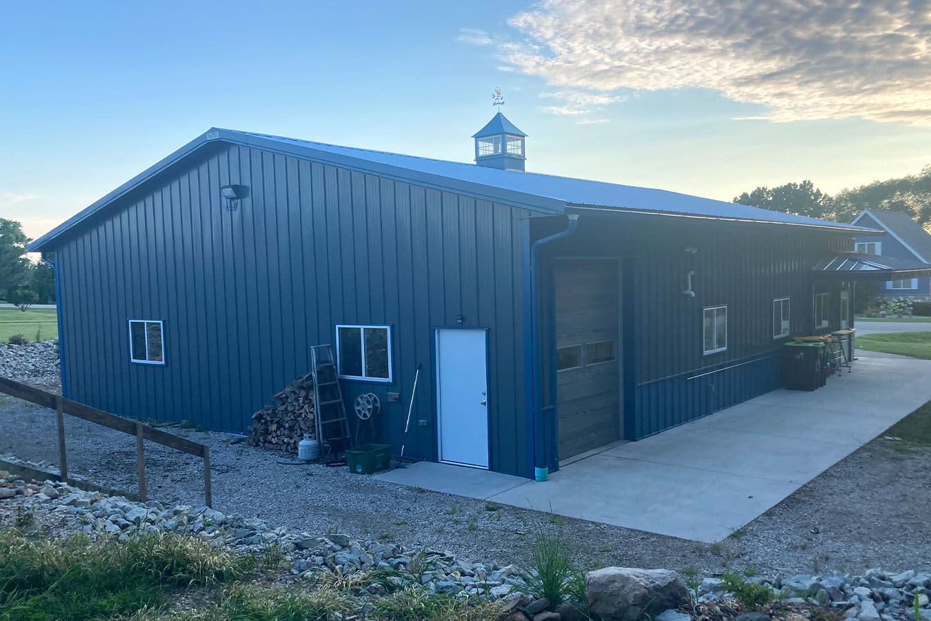 Lake house garage with blue steel siding, cupola, overhead door, and concrete driveway at sunset