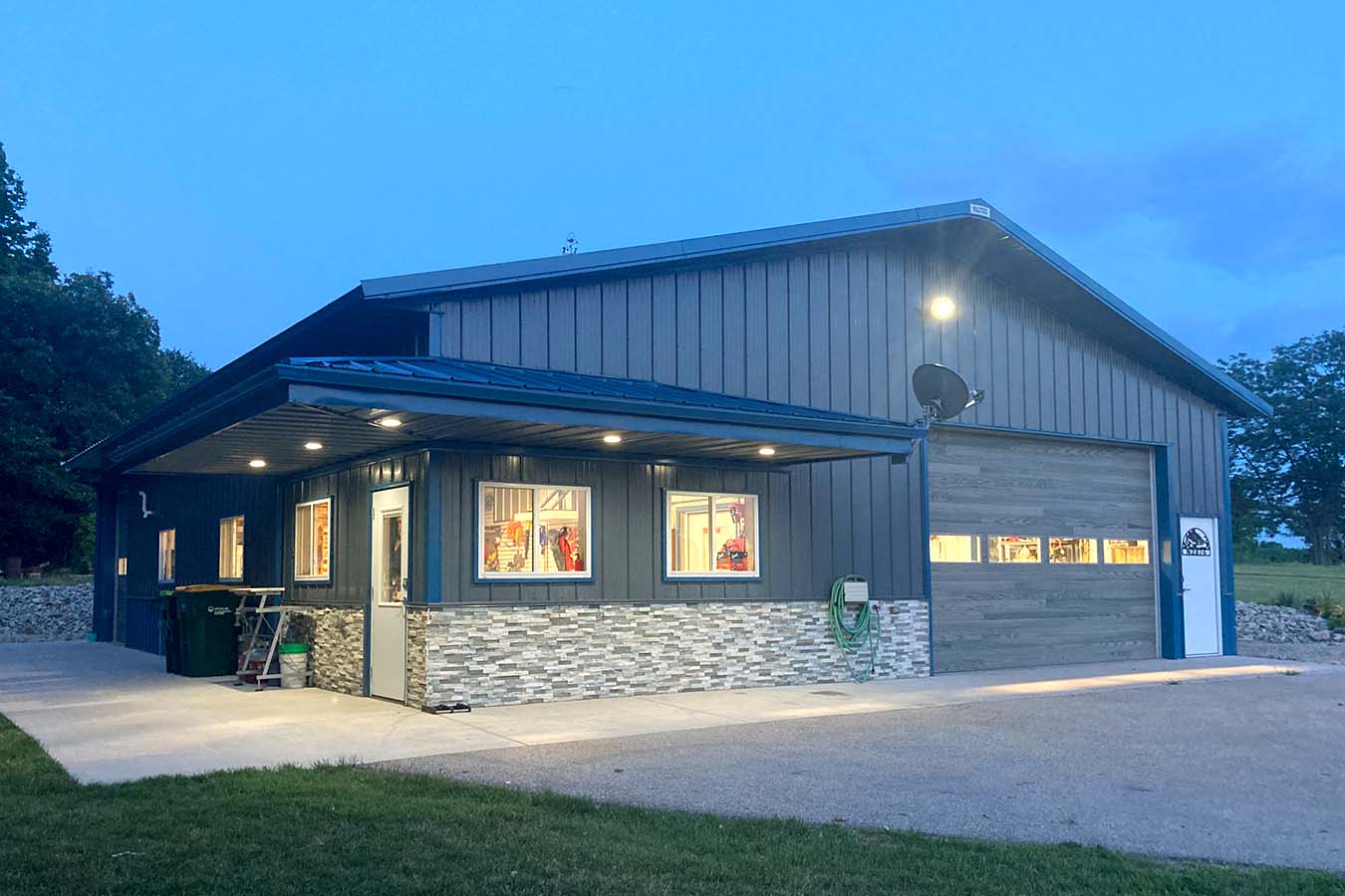 Lake house garage at dusk with covered patio, stone wainscot, and overhead garage door