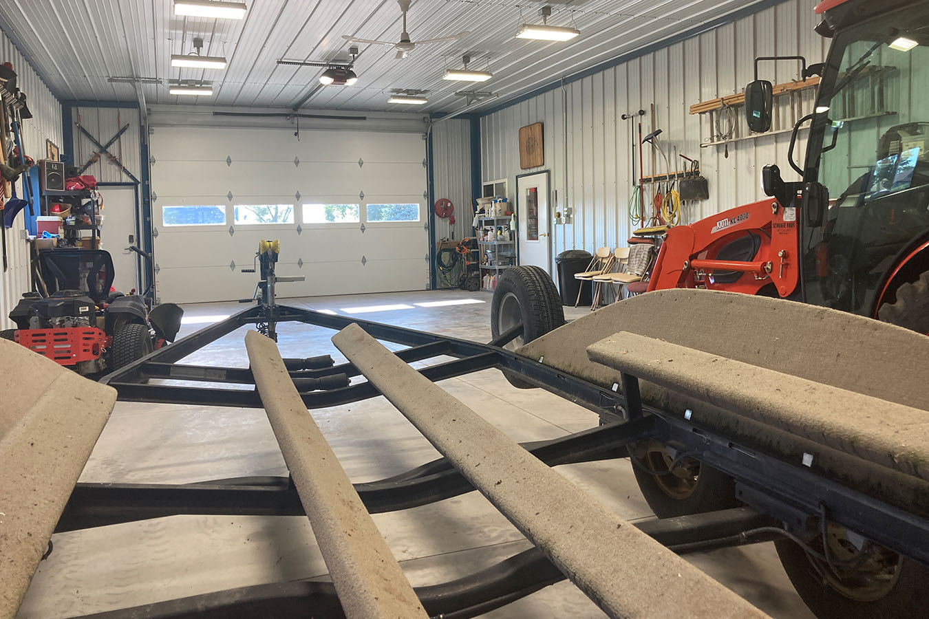 Lake house garage interior with boat trailer, tractor, overhead door, and steel liner walls