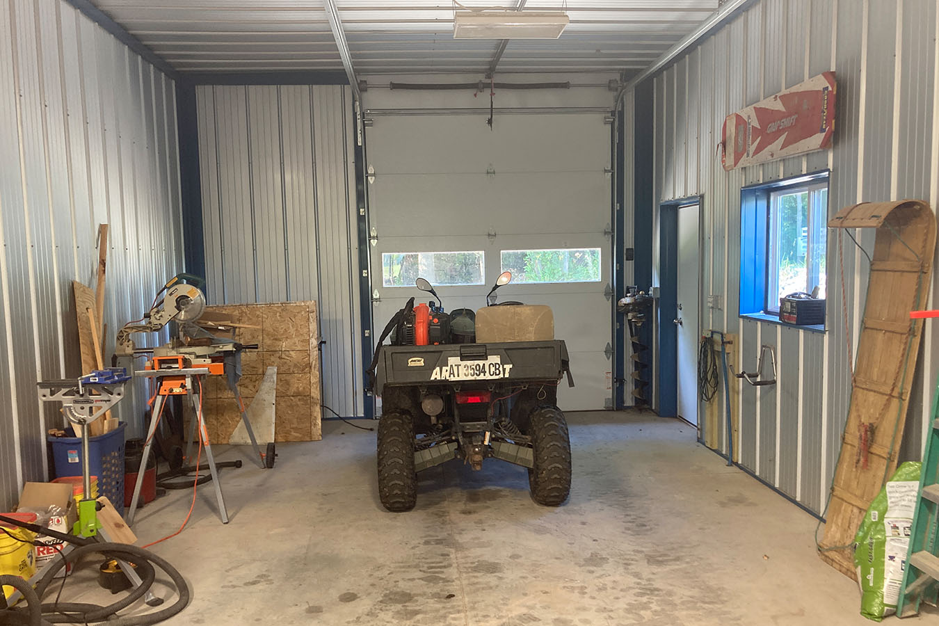 Lake house garage storage bay with ATV, overhead door, and workshop tools