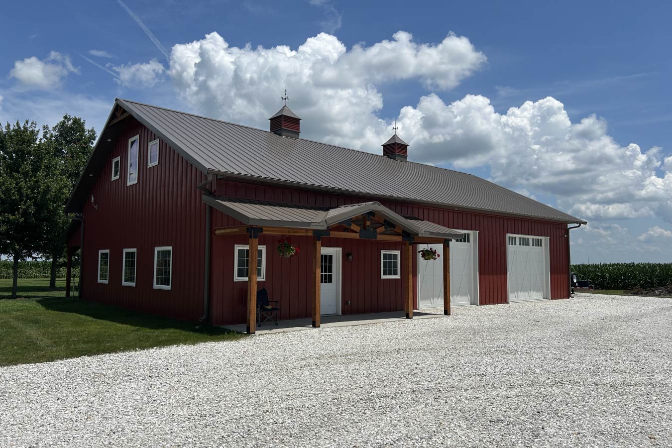 Residential workshop with red steel siding, steel roof, overhead garage doors, Plyco windows, covered porch, and cupolas 12' x 10' overhead doors for efficient access